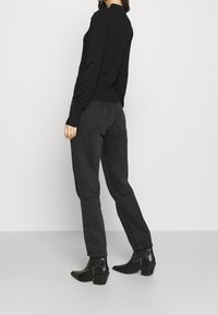 Czarny sweter z długimi rękawami i wysokim dekoltem, w połączeniu z ciemnymi spodniami z wysokim stanem. Czarne botki na kostkę z grubym obcasem dopełniają strój.