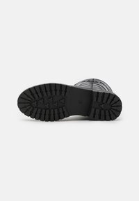 Suela de bota de goma negra con surcos y rieles profundos para tracción. La parte superior presenta un acabado texturizado y un elemento de diseño circular.