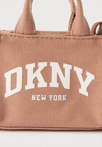 Rózsaszín texturált anyagból készült kézitáska fehér "DKNY" és "NEW YORK" felirattal. Két rövid fogantyúja van, és minimalista kialakítású.