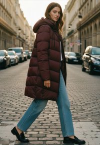 Tamsiai raudonas pūkinis paltas su gobtuvu, turintis stačiakampės formos siuvinėjimus. Derinamas su šviesiai mėlynomis tiesiomis kelnėmis ir juodomis loafers bateliais. Akmenimis grįsta gatvės aplinka.