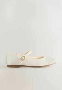 Pantof plat de balet, culoare crem, cu vârf rotund, curea la gleznă și accesorii decorative cu accent de perlă, partea superioară din țesătură texturată.