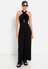 Melnā halter stila maksi kleita ar atslēgas caurumu priekšpusē, plecu pleķiem un pieguļošu vidukli. Valkāta ar masīviem melniem platformas sandalēm un saulesbrillēm.