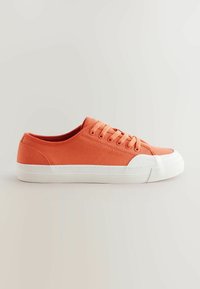 Oranssi kangaskenkä, jossa on valkoinen kumipohja, pyöreä kärki ja viisi nauhoitusaukkoa. Ominaisuuksina sileä pinta ja minimalistinen muotoilu.