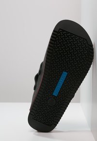Schwarze Gummisohle mit strukturiertem Grip-Muster. Blaues Etikett zeigt "BIRKENSTOCK" und Größe "39/250". Seitenansicht zeigt einen subtilen roten Akzent.