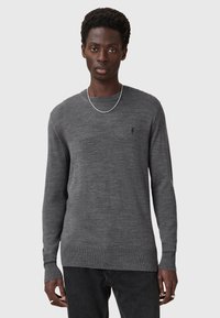Grauer Pullover mit langen Ärmeln, runder Halslinie und gerippten Bündchen. Verfügt über ein kleines, dezentes Logo auf der Brust. Glatte, weiche Textur.