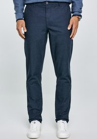 Pantalones azul marino con una textura suave, diseño ajustado, cierre de un botón y bolsillos laterales, combinados con zapatillas blancas.