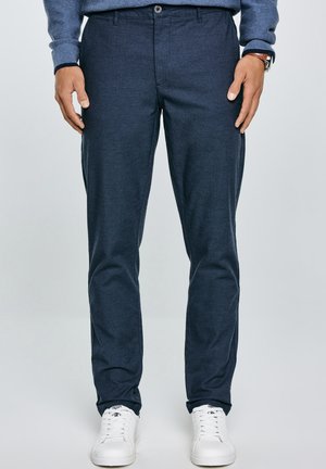Navyblauwe broek met een gladde textuur, slim fit ontwerp, enkele knoopsluiting en zijzakken, gecombineerd met witte sneakers.