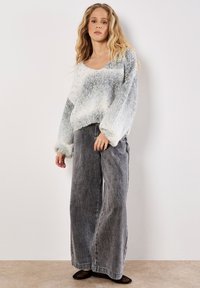 Sweter robiony na drutach w jasnoszarym kolorze z wielokolorowymi wstawkami, szerokie rękawy i krótki krój, w połączeniu z luźnymi szarymi dżinsami i czarnymi balerinami.