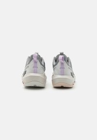 Une paire de baskets de sport grises et blanches avec des languettes de traction violettes claires, vue de l'arrière contre un fond blanc uni.