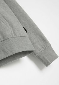 Szary sweter z ribbowymi mankietami i dołem, o gładkiej fakturze, z małą czarną metką logo po boku.