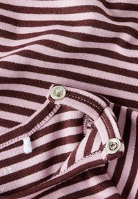 Paskowany materiał w odcieniach różu i brązu, z zapięciem na guzik z metalowym akcentem w odcieniu srebra. Miękka tekstura z widocznymi detalami szwów.