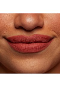 Matte läppstift i en varm terrakottaskugga applicerat på fylliga läppar, som visar en texturerad finish med fina linjer och naturliga läppkonturer.