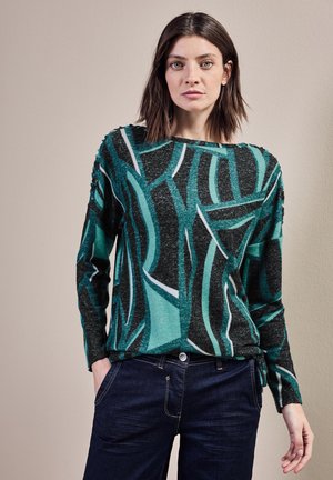 Pull à manches longues en teal foncé et noir avec des motifs abstraits verts et blancs. Présente une coupe décontractée et des fentes sur les côtés à l'ourlet.
