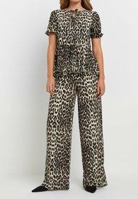 Completo in due pezzi con stampa leopardata, composto da una blusa con maniche corte e nodo al collo e pantaloni a gamba larga. Il tessuto è morbido e dalla texture liscia.