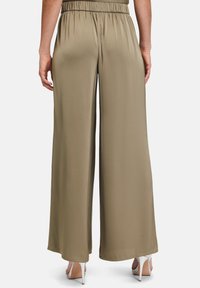 Szerokie spodnie w miękkim, oliwkowym kolorze, z elastycznym paskiem w talii i gładką teksturą, zestawione z srebrnymi szpilkami.