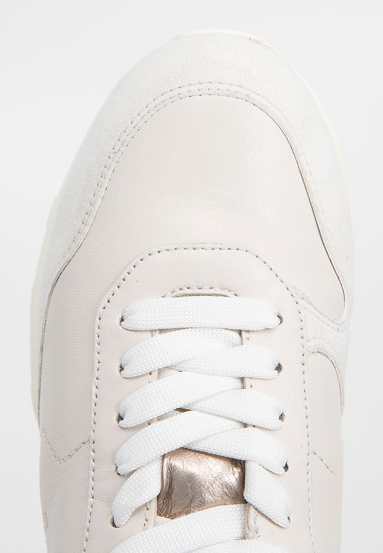 Sneaker beige chiaro in materiali in pelle e camoscio. Presenta lacci bianchi e una piastra di metallo vicino ai fori per i lacci. Forma della punta arrotondata.