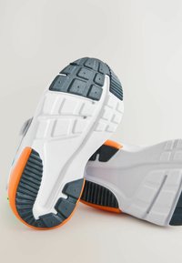 Weiße Sneaker mit einer strukturierten grauen Gummisohle, orangefarbenen Akzenten und gemustertem Profil. Verfügt über ein modernes Design mit leichter Krümmung.