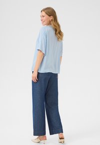 Blusa azzurro chiaro, fluente, con maniche ampie, abbinata a jeans a gamba larga blu scuro. Tacchi beige. Design semplice e minimalista. Tessuto liscio.