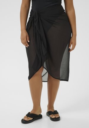 Svart genomskinlig sarong med knuten midja, som har en lätt, flödande textur och en hög sprunddesign. Matta sandaler fulländar looken.