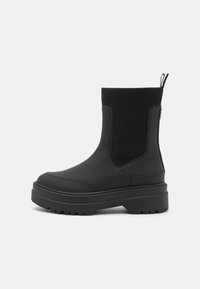 Bottines noires avec une tige en caoutchouc lisse, des détails texturés à côtes, des panneaux latéraux élastiques et une semelle épaisse.