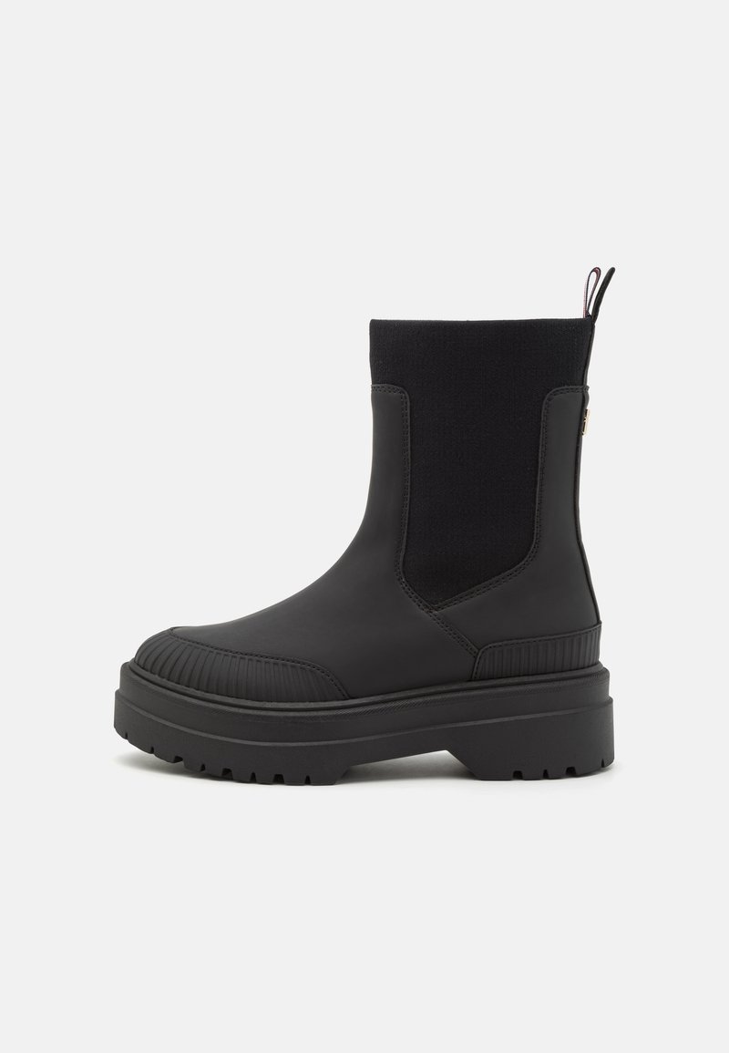 Bottines noires avec une tige en caoutchouc lisse, des détails texturés à côtes, des panneaux latéraux élastiques et une semelle épaisse.