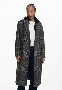 Cappotto doppiopetto in tessuto grigio a quadri con accenti rossi, ampi revers e cappuccio. Realizzato in tessuto texturizzato, presenta una silhouette sagomata.