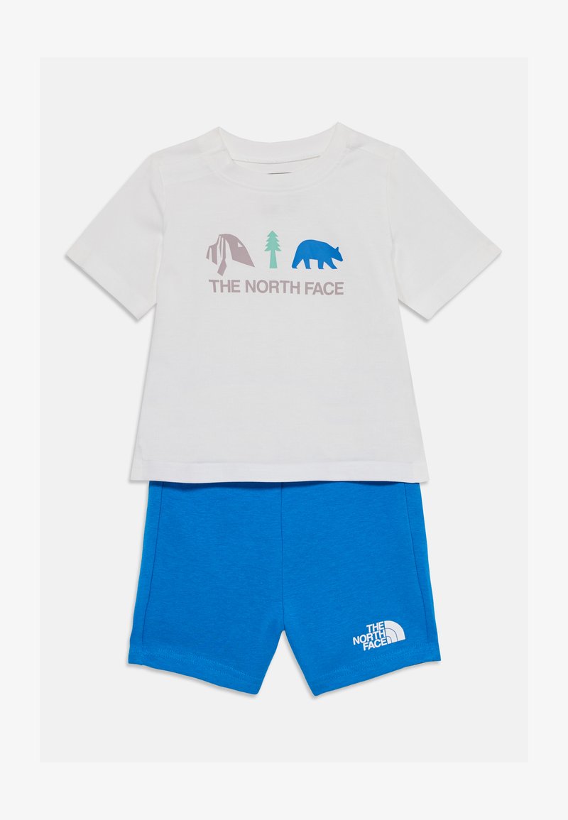 Biely bavlnený tričko s grafikou kempovania, stromu a medveďa v purpurovej a modrej farbe, spárované s modrými šortkami s bielym logom.