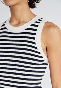 Ribbed tank top with navy and white horizontal stripes, featuring a round neckline and wide armholes. Soft fabric with a textured finish.