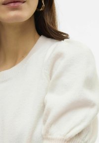 Valge kudumisega sviiter, millel on ümar kaelus ja puffdetaljidega varrukad. Pehme tekstuur ribide aksentidega mansettidel ja allservas.