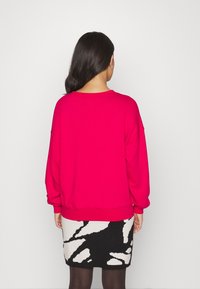 Roze oversized sweatshirt met losse mouwen, gecombineerd met een zwart-wit gestreepte rok. Soepele stof en relaxed fit.