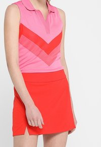 Ärmlös pikétröja i rosa med rött chevronmönster, kombinerad med en enfärgad röd skirtshorts. Båda tillverkade av andningsbart tyg.