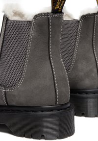 Gros plan sur des bottines en daim gris avec des semelles épaisses noires rainurées, des panneaux latéraux élastiques, des coutures blanches et une doublure en polaire au sommet.