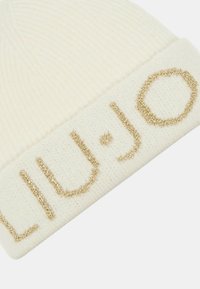 Kremowa dziana czapka z prążkowanym texturem i naszytym złotym logo "LIU·JO" z przodu. Okrągła korona, miękki materiał.