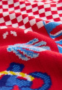 Tejido de punto con un patrón a cuadros en rojo y blanco, y acentos en azul y blanco. Formas y texturas distintivas crean un interés visual.