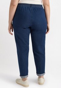 Granatowe dżinsy z elastycznym pasem, luźny krój, podwinięte mankiety i zestawione z beżowymi trampkami. Tkanina wydaje się lekko teksturowana.