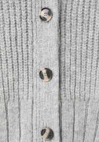 Suéter gris tejido con costillas verticales, cinco grandes botones con un patrón jaspeado y una tela suave y texturizada.