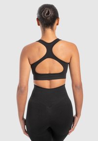 Schwarzer Sport-BH mit Rückenausschnitt und Cut-Out-Details. Der Stoff wirkt dehnbar und wird mit hochgeschnittenen schwarzen Leggings kombiniert.