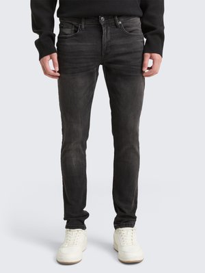 Jean noir en denim avec une coupe slim, design à cinq poches, décoloration subtile et garnitures en métal, associés à des baskets blanches.