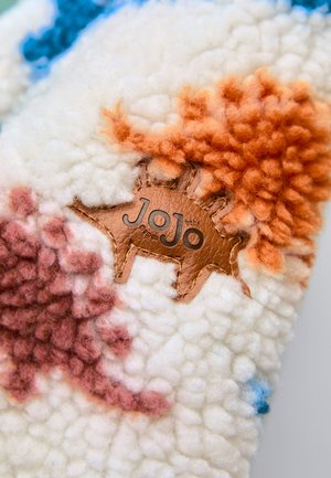 Zacht gestructureerde stof met een gestikte bruine leren patch in de vorm van een dier, met het "JoJo"-merk omringd door kleurrijke wollen plukjes.