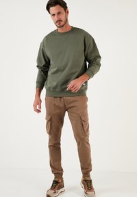 Sudadera verde oliva con cuello redondo y puños de canalé, combinada con pantalones cargo beige que cuentan con bolsillos laterales y puños elásticos.