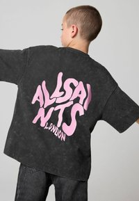 Sort oversized T-shirt med en slidt tekstur, med fed pink tekst "ALLSAINTS LONDON" på ryggen, korte ærmer og en afslappet pasform.