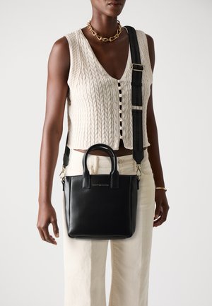 Black leather tote bag with dual top handles and a detachable shoulder strap. Features a gold logo accent on the front and rectangular shape.