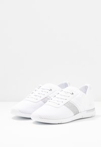 Vita atletiska skor i stickad textil, med ett silverfärgat rand, snörningsdesign och rund tå. Lätt och flexibel sula.