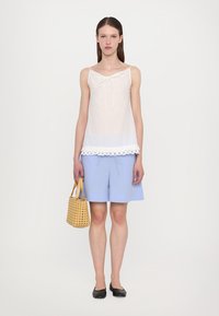 White sleeveless top with a lace trim and drawstring, paired with light blue striped shorts. Holding a woven yellow handbag, black flats worn.