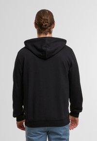 Zwarte hoodie gemaakt van zacht stof, met een kangoeroezak, ribbels aan de mouwen en onderkant, gezien van de achterkant.