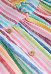 Prim-plan al unui material cu dungi verticale multicolore și două nasturi din lemn cusute într-o cusătură a unui articol vestimentar.