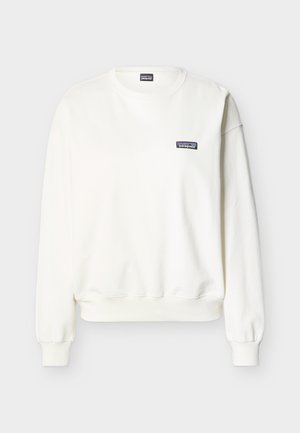 Biała bluza z długim rękawem i okrągłym dekoltem, z prążkowanymi mankietami i ściągaczem u dołu, z małą naszywką z logo Patagonia na lewej piersi.