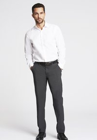 Camicia bianca button-up, pantaloni neri su misura e scarpe nere. La camicia ha una texture liscia; i pantaloni hanno un taglio dritto classico.