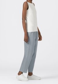 Vit ärmlös topp parat med ljusgrå byxor. Tyget verkar slätt och lätt. Vita sneakers fulländar outfitten.