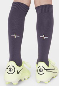 Calze viola fino al ginocchio con bordi a coste presentano un ricamo di croce multicolore. Indossate con scarpe da calcio gialle vivaci.